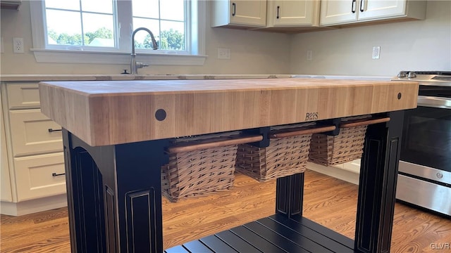 kitchen featuring butcher block countertops, light hardwood / wood-style flooring, a kitchen island, and white cabinets