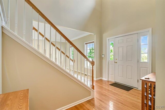 foyer entrance with ornamental molding, a wealth of natural light, light wood-type flooring, and a towering ceiling