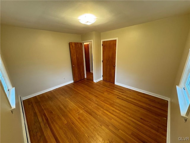 unfurnished room with baseboard heating, wood finished floors, and baseboards