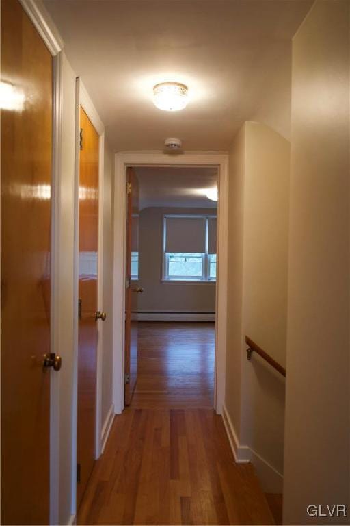 hallway featuring baseboards, a baseboard heating unit, and wood finished floors