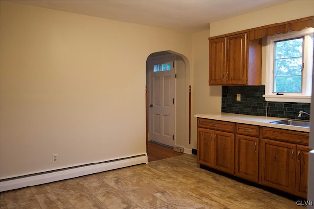 kitchen featuring a baseboard radiator, arched walkways, brown cabinetry, and a sink