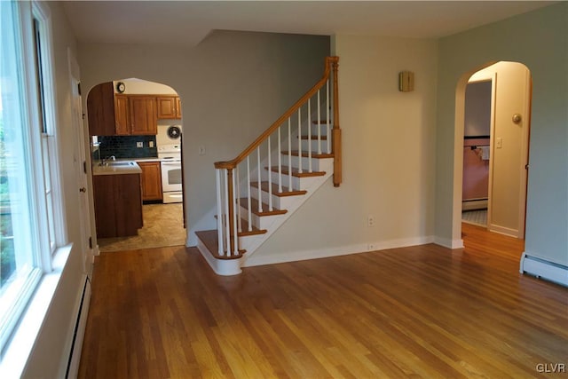 stairs featuring baseboards, a baseboard radiator, arched walkways, and wood finished floors