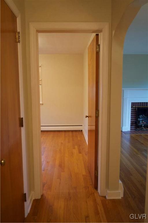 hall with a baseboard heating unit, arched walkways, baseboards, and wood finished floors