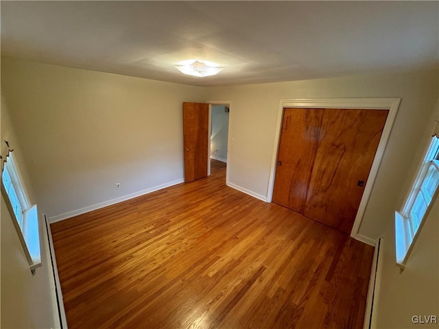 unfurnished bedroom with a closet, baseboard heating, wood finished floors, and baseboards