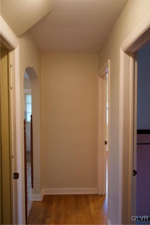 hall featuring arched walkways, wood finished floors, and baseboards