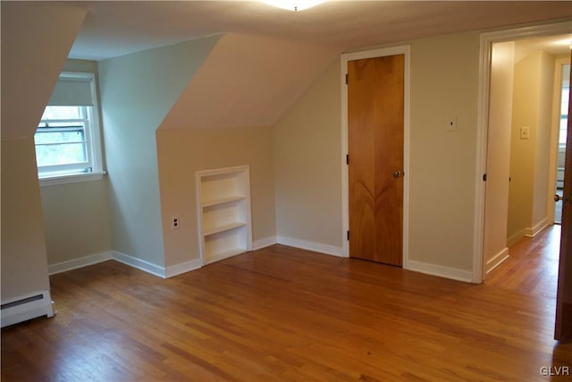 additional living space featuring a baseboard heating unit, baseboards, built in features, and wood finished floors