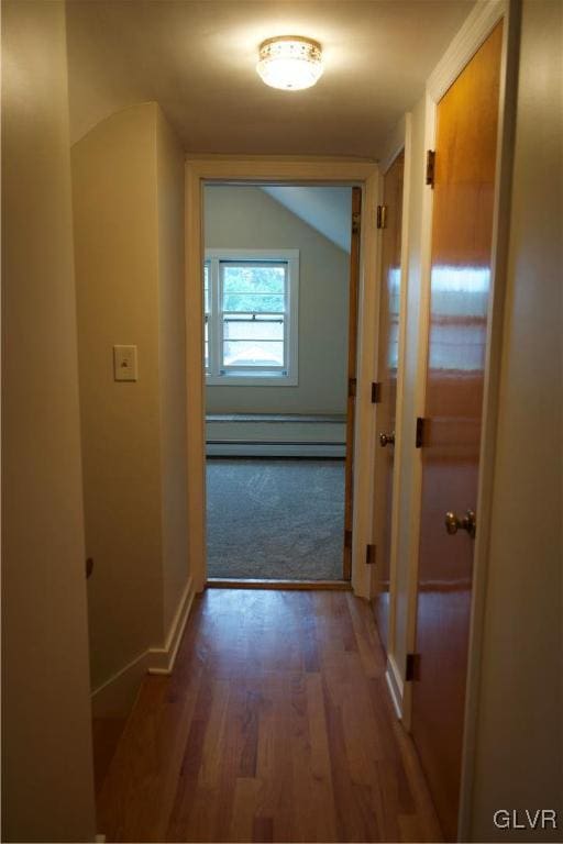 corridor featuring vaulted ceiling, baseboard heating, wood finished floors, and baseboards