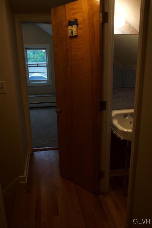 hallway featuring a baseboard heating unit, a sink, and wood finished floors