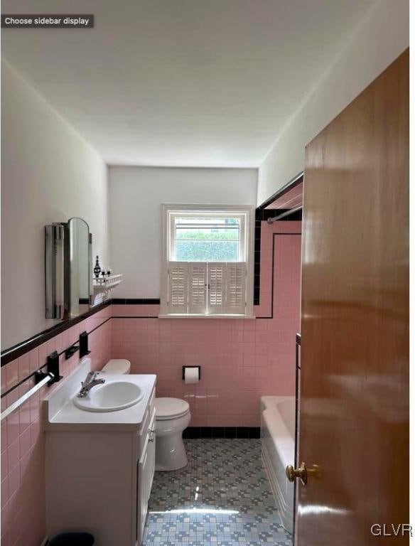 full bath with a bathtub, tile walls, toilet, wainscoting, and vanity