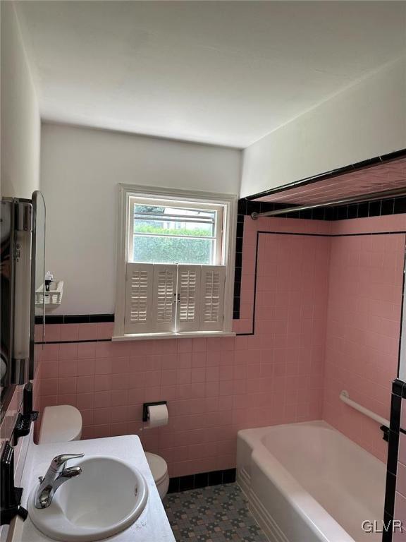 full bath featuring a bathing tub, toilet, a wainscoted wall, a sink, and tile walls