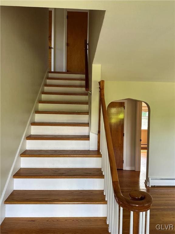 stairway with arched walkways, a baseboard heating unit, wood finished floors, baseboards, and baseboard heating