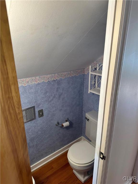 bathroom with baseboards, vaulted ceiling, toilet, and wood finished floors