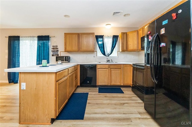 kitchen with sink, kitchen peninsula, black appliances, and light hardwood / wood-style floors