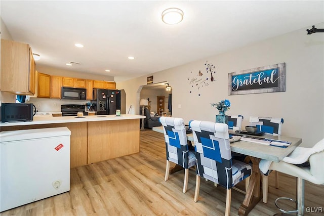 kitchen featuring light brown cabinetry, black appliances, kitchen peninsula, and light wood-type flooring