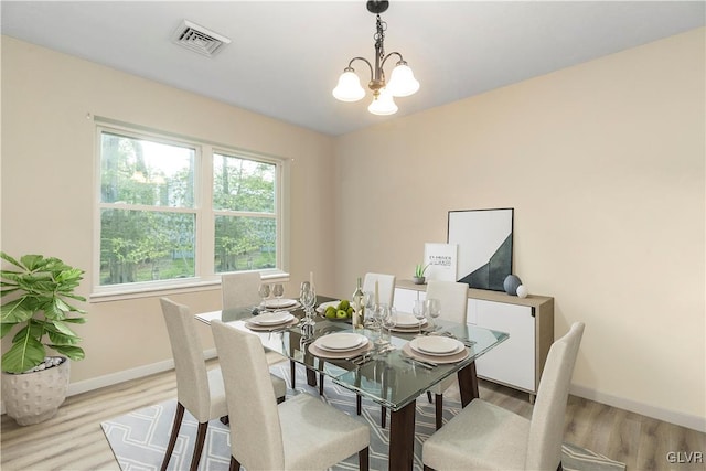 dining area with light hardwood / wood-style floors and an inviting chandelier