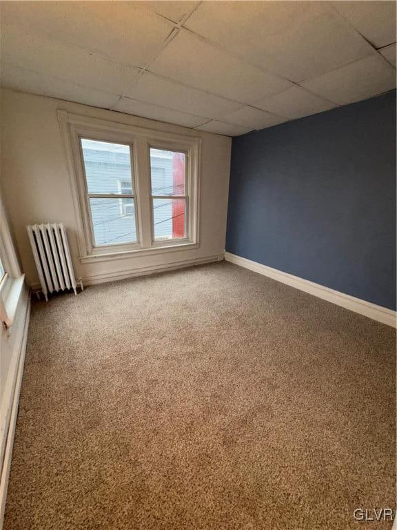 carpeted spare room featuring radiator heating unit and a drop ceiling