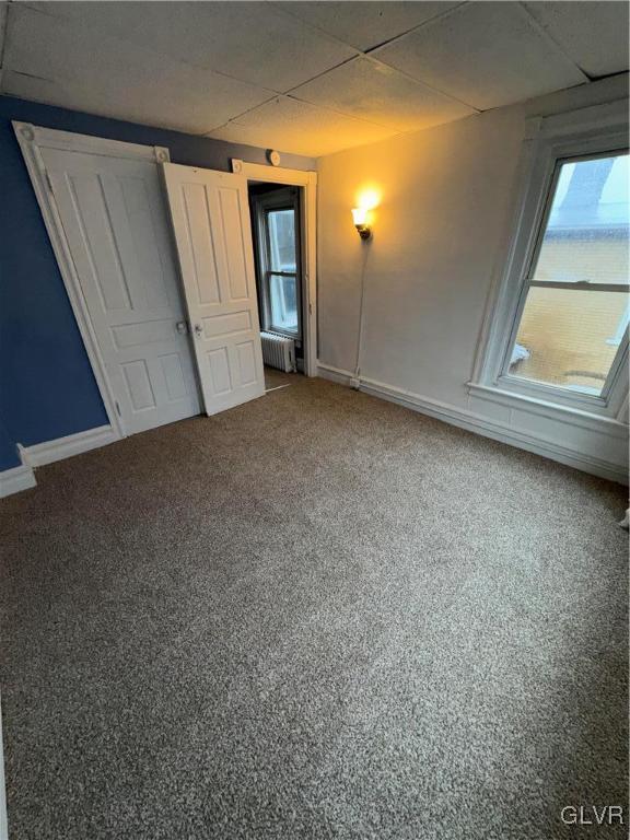 unfurnished bedroom featuring a paneled ceiling, radiator, and carpet floors