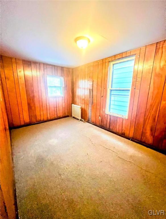 spare room with light carpet, radiator, and wooden walls