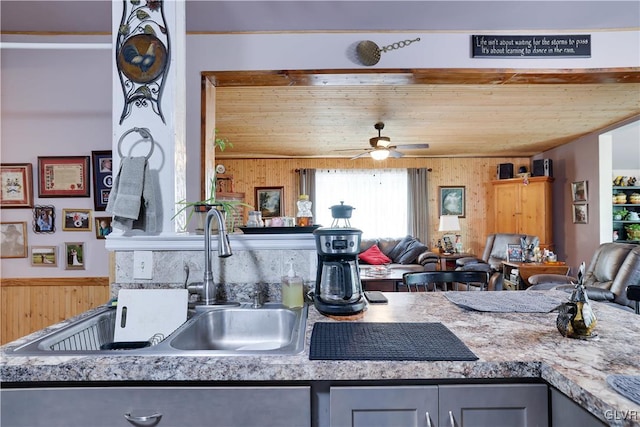 kitchen featuring gray cabinetry, ceiling fan, sink, and wooden walls