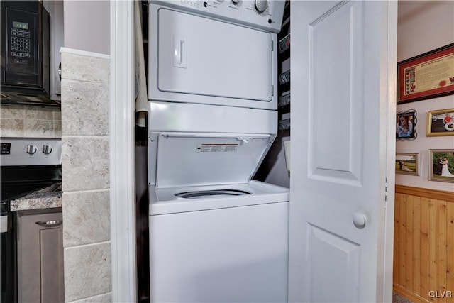 laundry area featuring stacked washer and dryer and wood walls