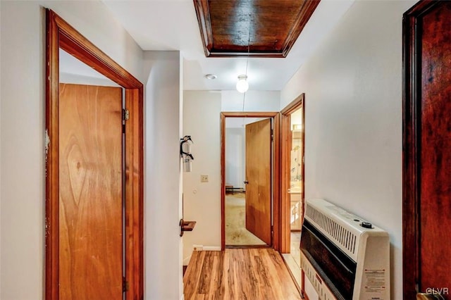 hallway with ornamental molding, heating unit, a tray ceiling, and light hardwood / wood-style floors