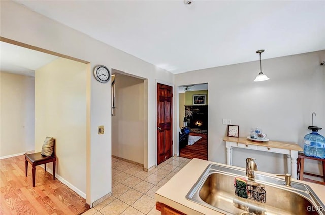 kitchen featuring pendant lighting, light wood-type flooring, sink, and a brick fireplace