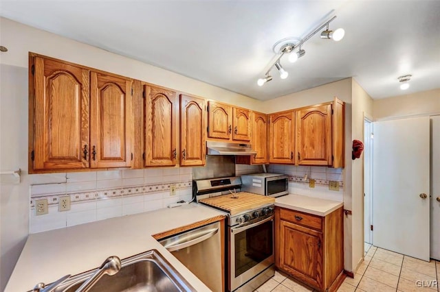 kitchen featuring backsplash, sink, light tile patterned floors, and appliances with stainless steel finishes