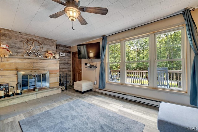 unfurnished room with light hardwood / wood-style flooring, ceiling fan, wooden walls, a stone fireplace, and a baseboard heating unit