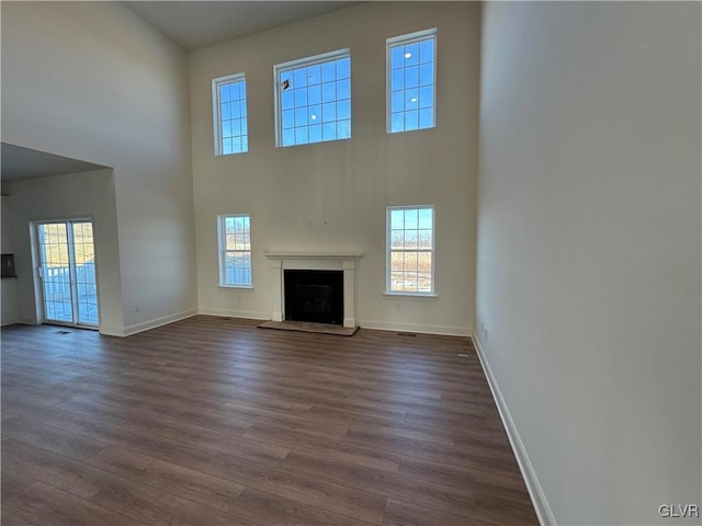 unfurnished living room featuring a towering ceiling, a healthy amount of sunlight, and dark hardwood / wood-style flooring