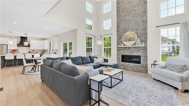 living room with sink, a fireplace, light hardwood / wood-style flooring, and a towering ceiling