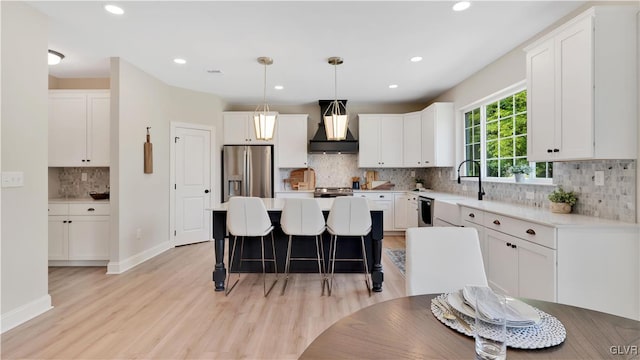 kitchen with tasteful backsplash, white cabinetry, stainless steel fridge with ice dispenser, light hardwood / wood-style floors, and premium range hood