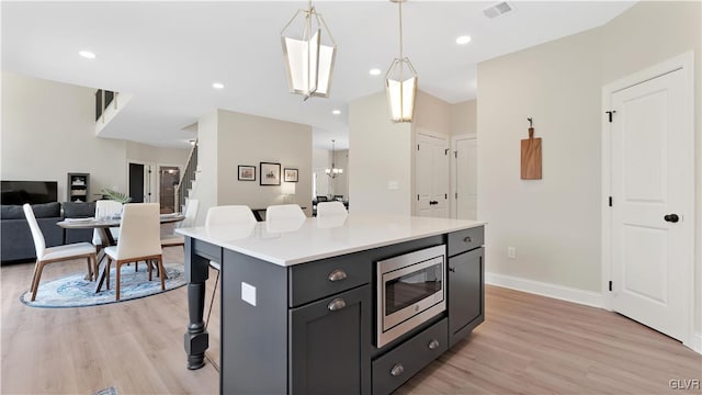 kitchen featuring a center island, light wood-type flooring, a breakfast bar, stainless steel microwave, and decorative light fixtures