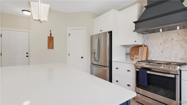 kitchen with appliances with stainless steel finishes, white cabinets, custom range hood, pendant lighting, and tasteful backsplash