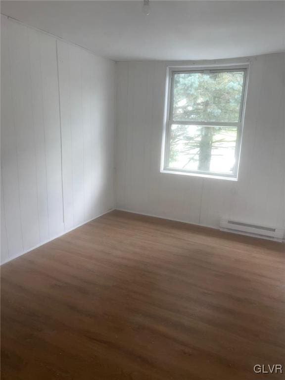 empty room featuring baseboard heating and dark wood-type flooring