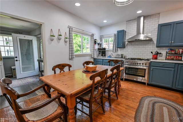 kitchen with wall chimney range hood, double oven range, blue cabinets, light wood-type flooring, and tasteful backsplash