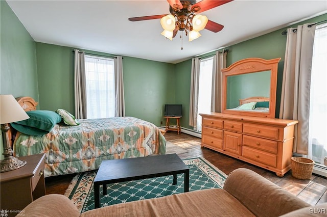 bedroom with ceiling fan, baseboard heating, wood-type flooring, and multiple windows