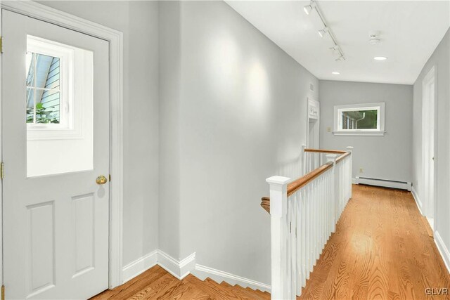 hallway featuring vaulted ceiling, a baseboard heating unit, track lighting, and light wood-type flooring