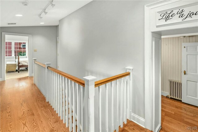 hallway with rail lighting, radiator heating unit, lofted ceiling, and light hardwood / wood-style floors