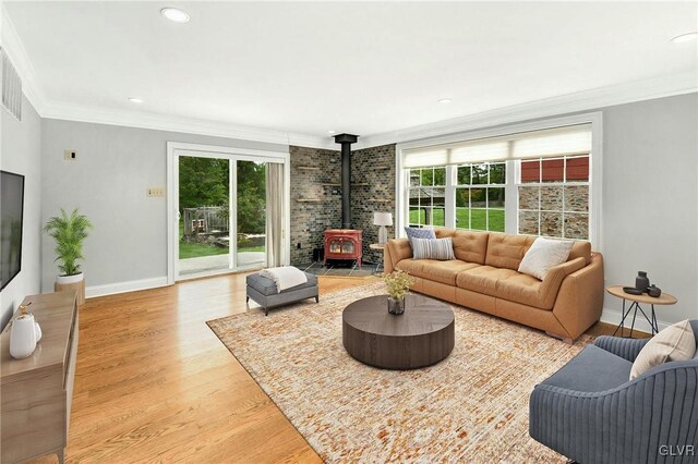 living room with light wood-type flooring, crown molding, brick wall, and a wood stove