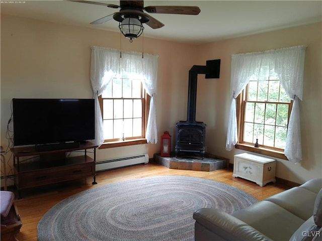 living room with ceiling fan, wood-type flooring, a wood stove, and baseboard heating