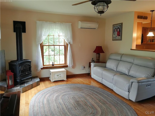 living room featuring ceiling fan, light hardwood / wood-style floors, a wood stove, and a wall mounted air conditioner