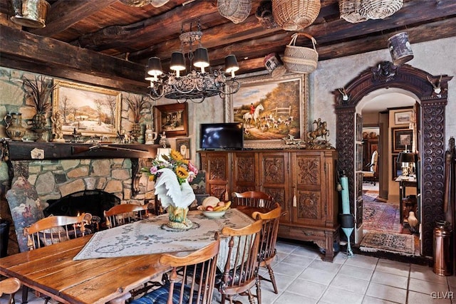 tiled dining room with a notable chandelier, wood ceiling, beamed ceiling, and a stone fireplace