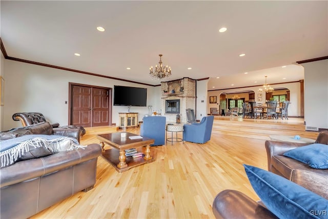 living room with a notable chandelier, light hardwood / wood-style floors, a large fireplace, and ornamental molding