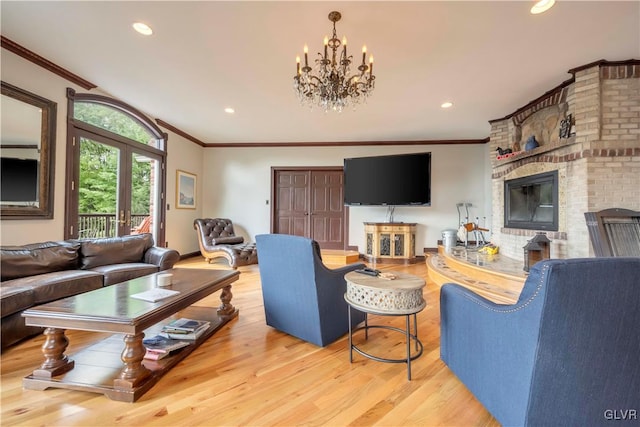 living room with a notable chandelier, ornamental molding, a fireplace, light hardwood / wood-style flooring, and brick wall