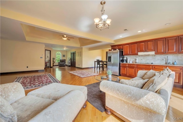 living room featuring light hardwood / wood-style floors, ceiling fan with notable chandelier, sink, and a raised ceiling