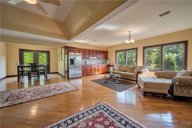 living room with a wealth of natural light, ceiling fan with notable chandelier, and light wood-type flooring