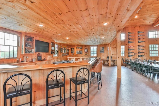 kitchen featuring wood ceiling, a breakfast bar area, wooden walls, and concrete floors