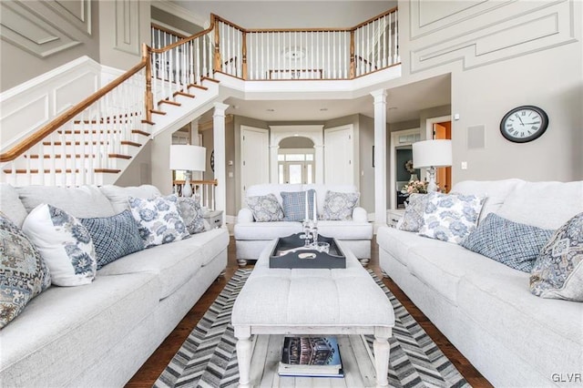 living room featuring dark wood-type flooring, ornate columns, and a towering ceiling