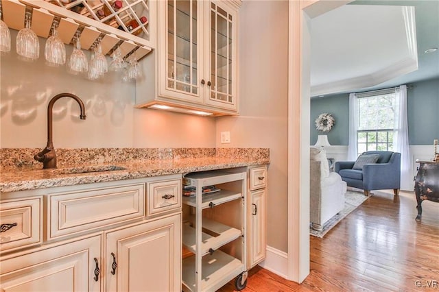 bar with light stone countertops, ornamental molding, sink, and light hardwood / wood-style flooring