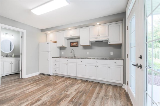 kitchen featuring light wood-type flooring, white refrigerator, a wealth of natural light, and dark stone countertops